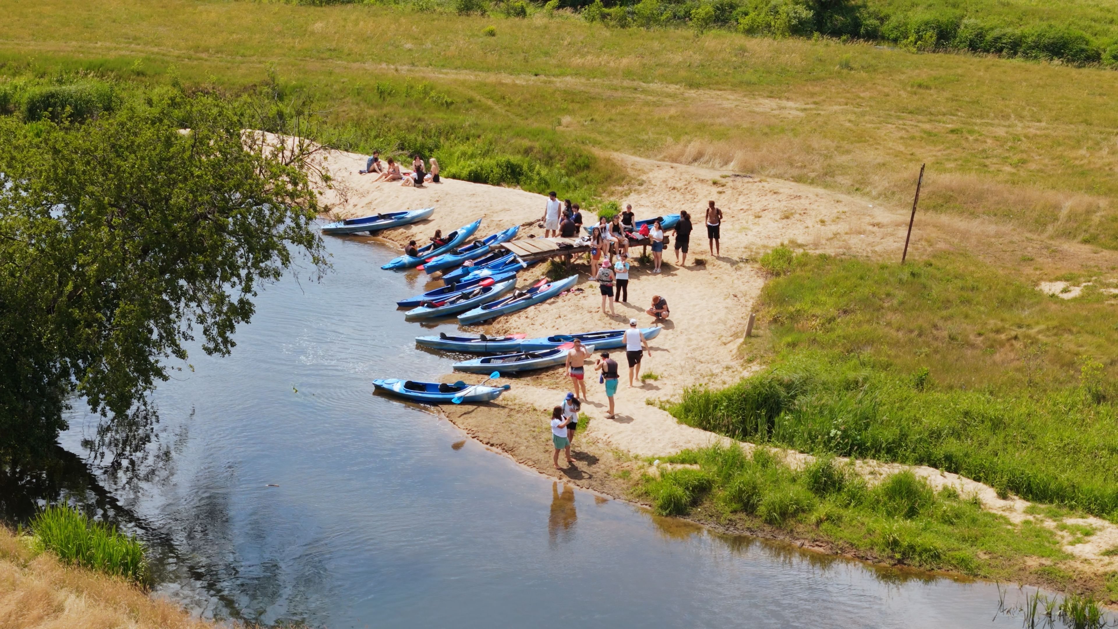 A group of students preparing kayaks on a riverbank before the trip.