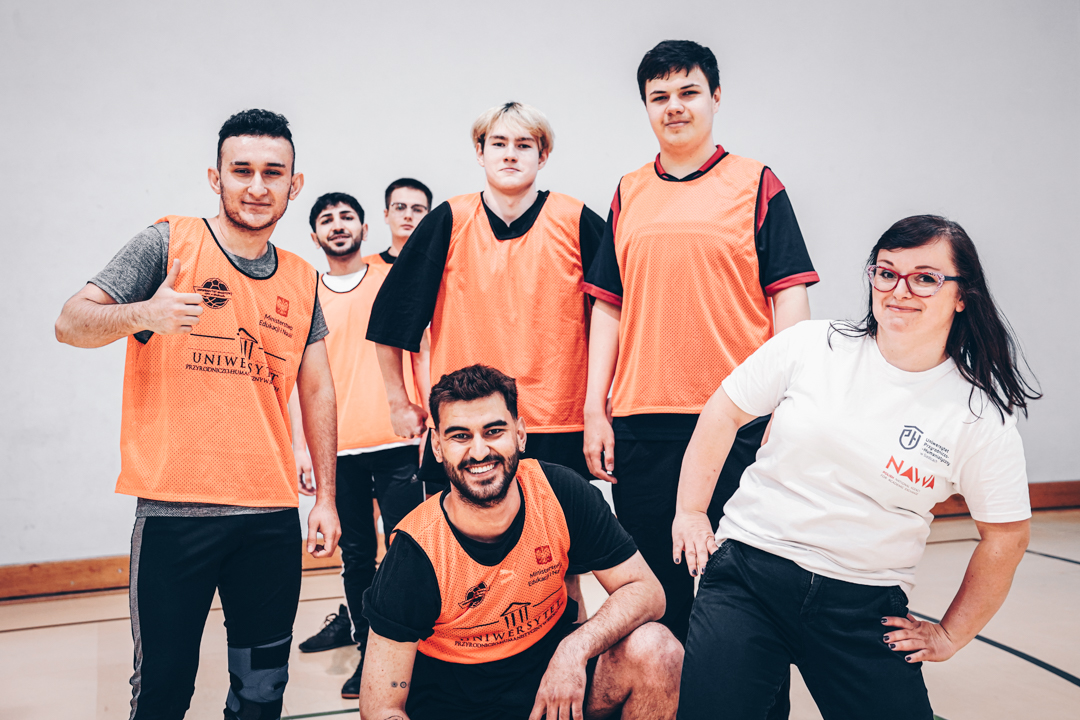Drużyna męska wraz z koordynatorką erasmus stoją w strojach sportowych i pozują do zdjęcia.