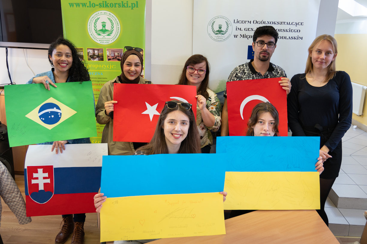Students holding colorful posters with flags of various countries during a high school visit.
