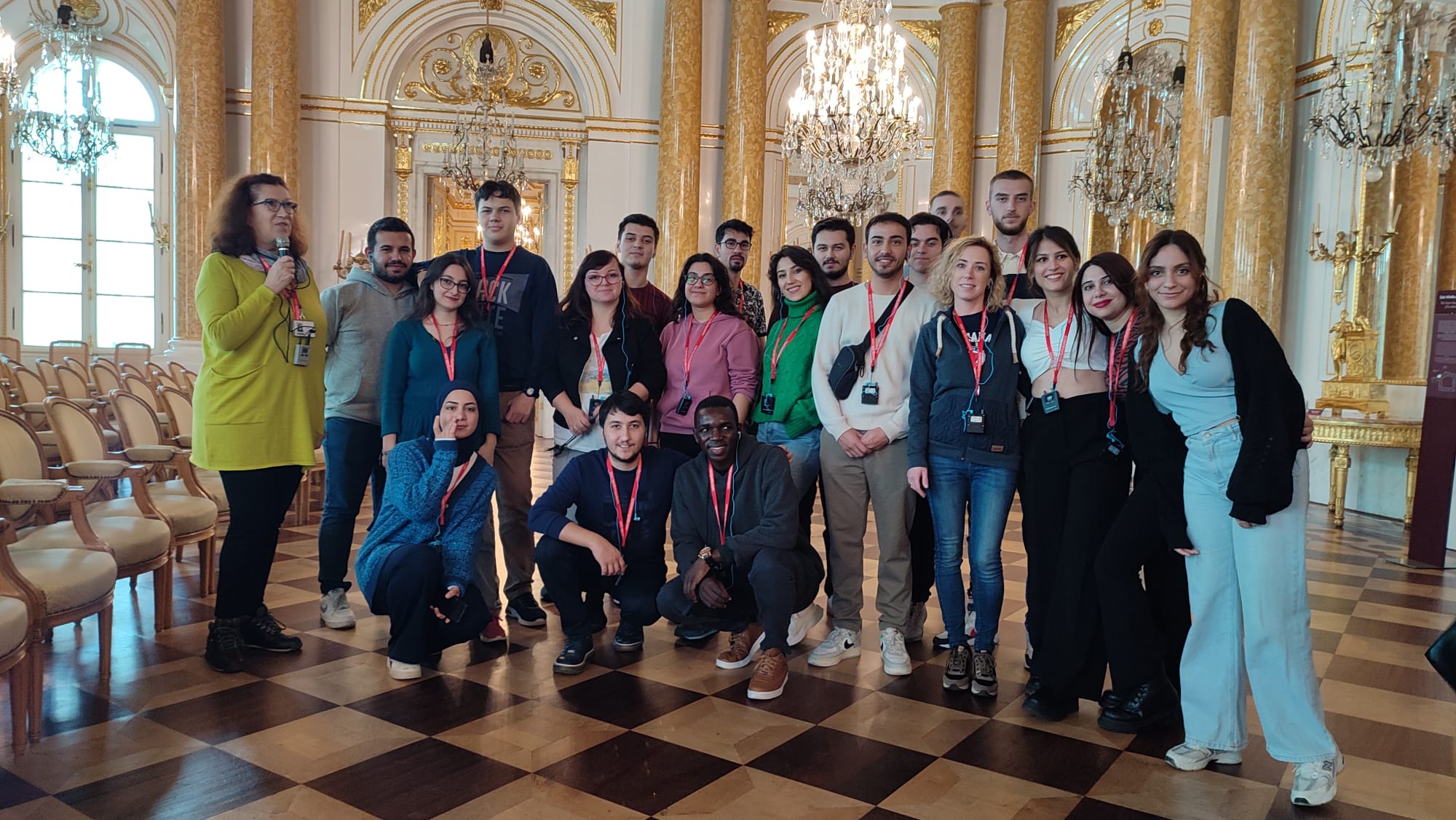 Erasmus+ students posing in a hall with ornate golden columns and chandeliers in Warsaw.