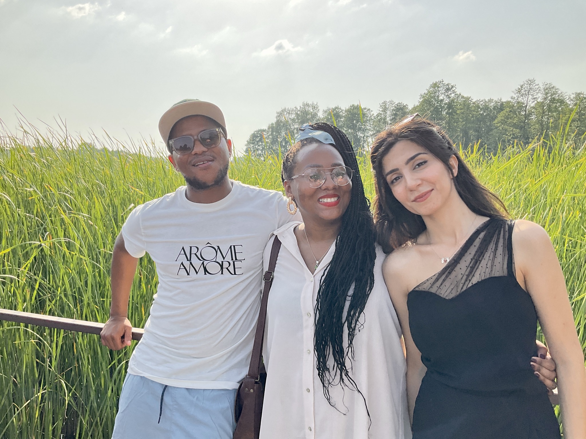 Three students posing in front of green reeds during a farewell meeting.